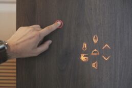 Hand touches illuminated button on smart home interface. Alchimia invisible interior technolgoy vbh