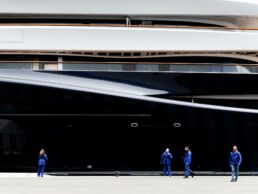 Workers beside a large, modern yacht