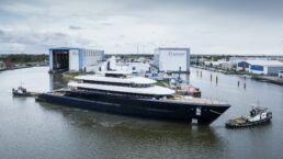 Feadship Project 1012 Superyacht. Large yacht at shipyard with tugboats.