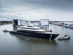 Feadship Project 1012 Superyacht. Large yacht at shipyard with tugboats.